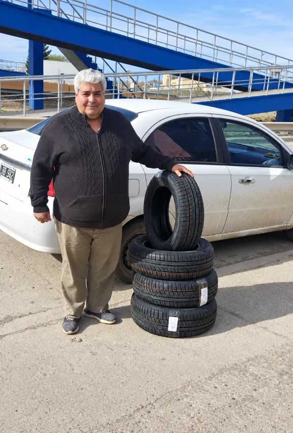 Un cliente con cubiertas junto a su auto frente a un puente azul